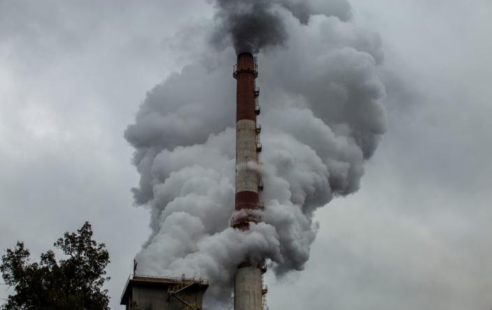Unter dem bedeckten Himmel betrachtet, steigen Rauchschwaden aus dem Schornstein einer rot-weißen Fabrik.